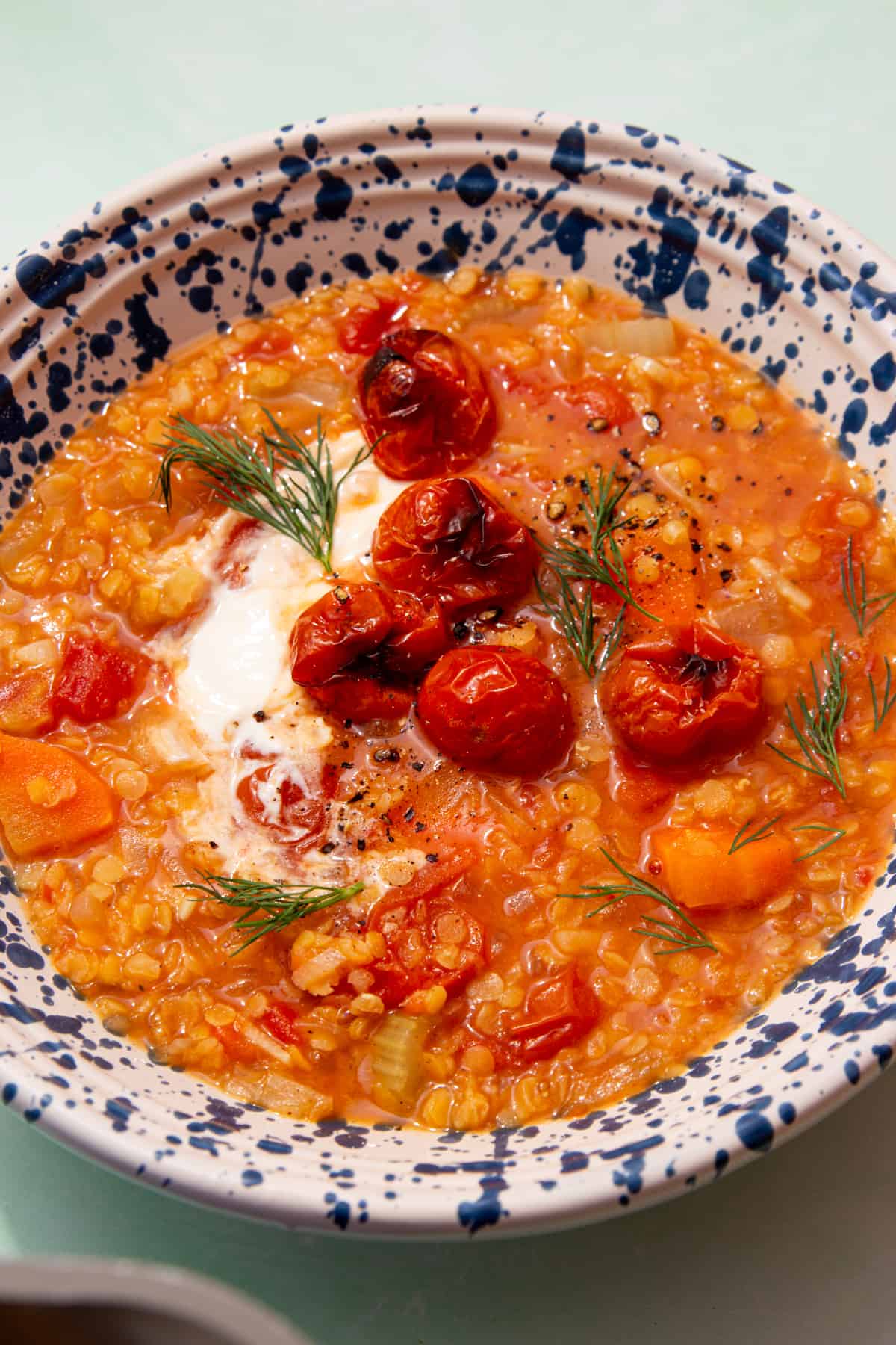 A patterned bowl full of red lentil soup with carrots, roasted cherry tomatoes, some dill and a dollop of creme fraiche.
