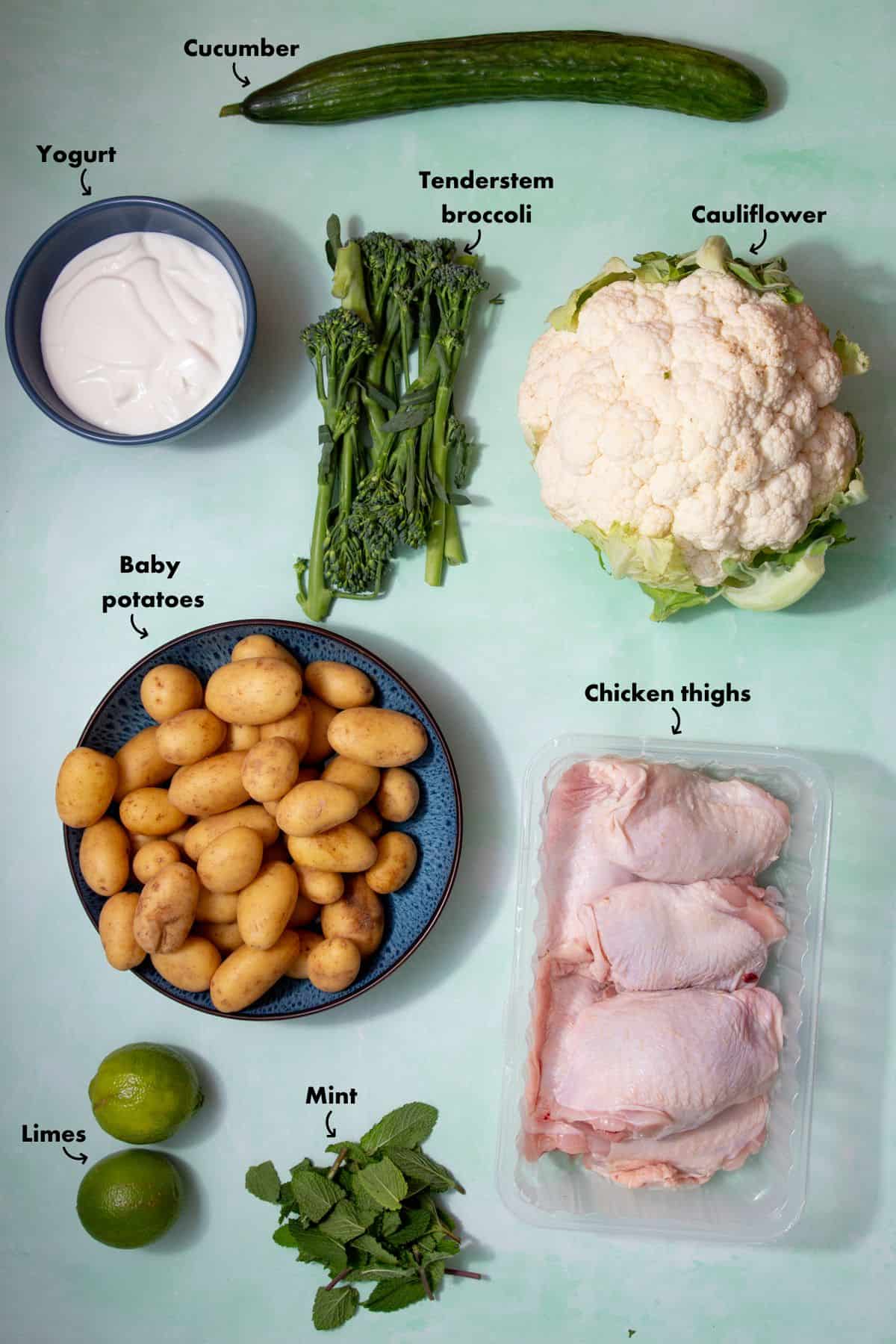 Ingredients to make the cauliflower and chicken tray bake laid out on a pale blue background and labelled.