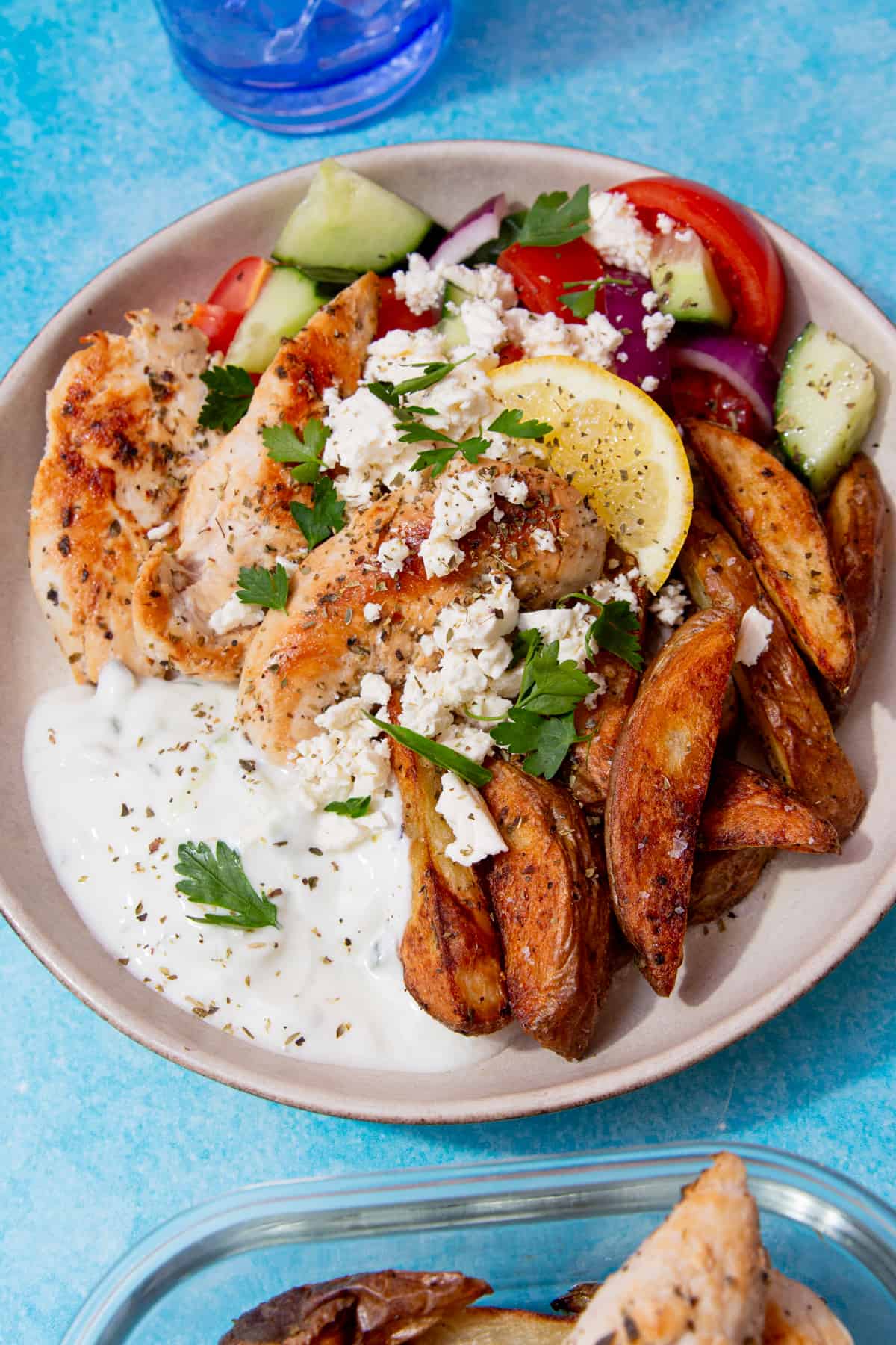 A bowl of salad with golden browned chicken pieces, fries, tzatziki, topped with feta and a wedge of lemon.