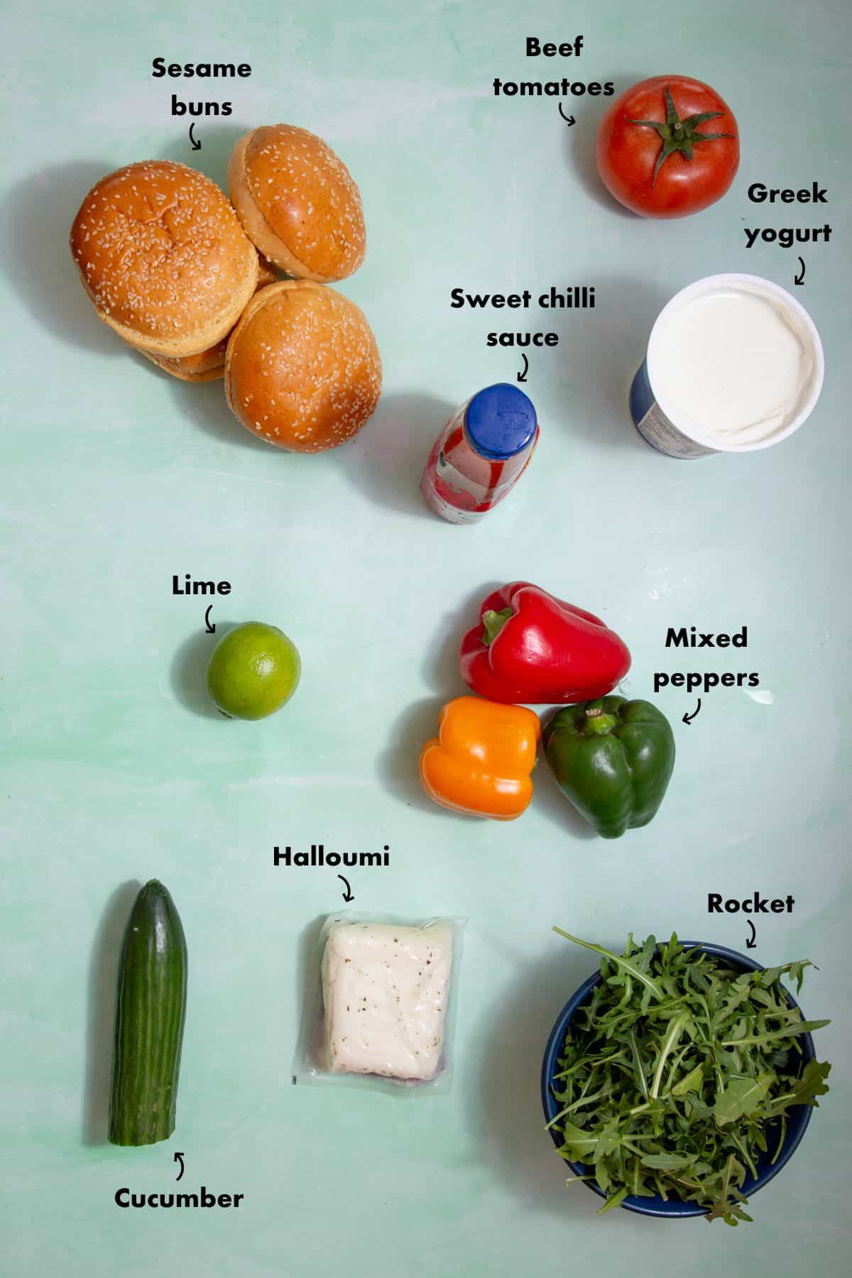 Ingredients to make halloumi burgers laid out on a pale blue background and labelled.
