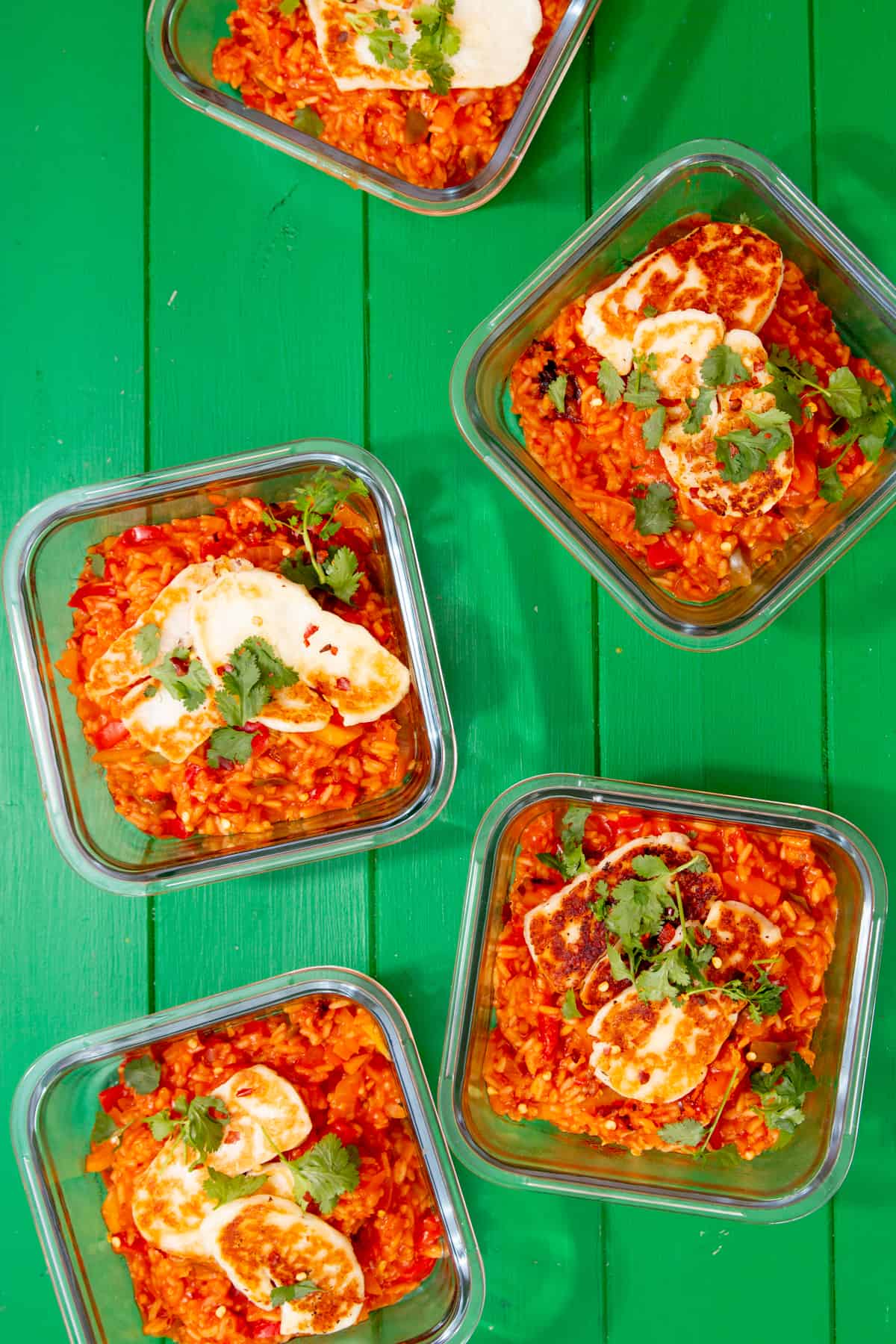 5 meal prep containers with tomatoey rice and browned halloumi slices on top and fresh coriander.