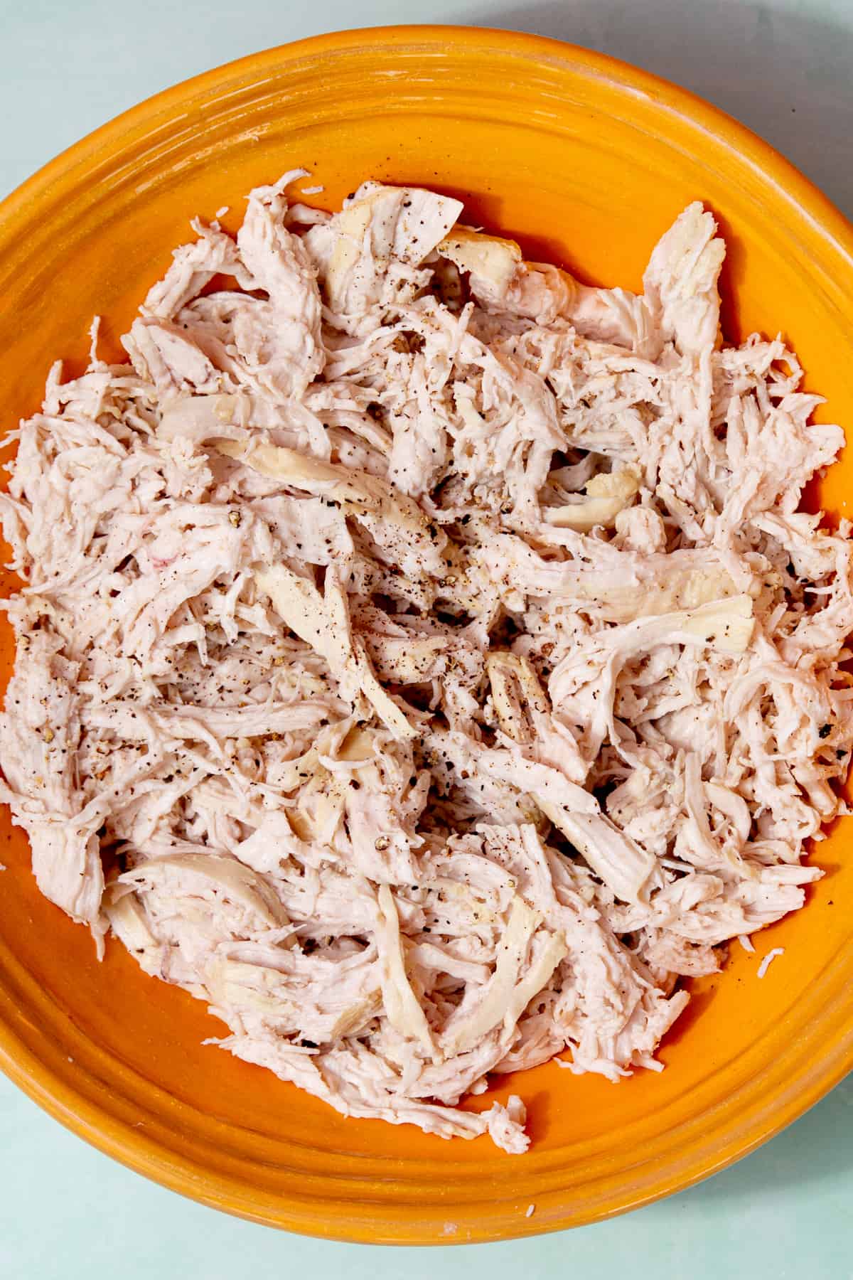 A yellowish plate with lots of seasoned shredded chicken.