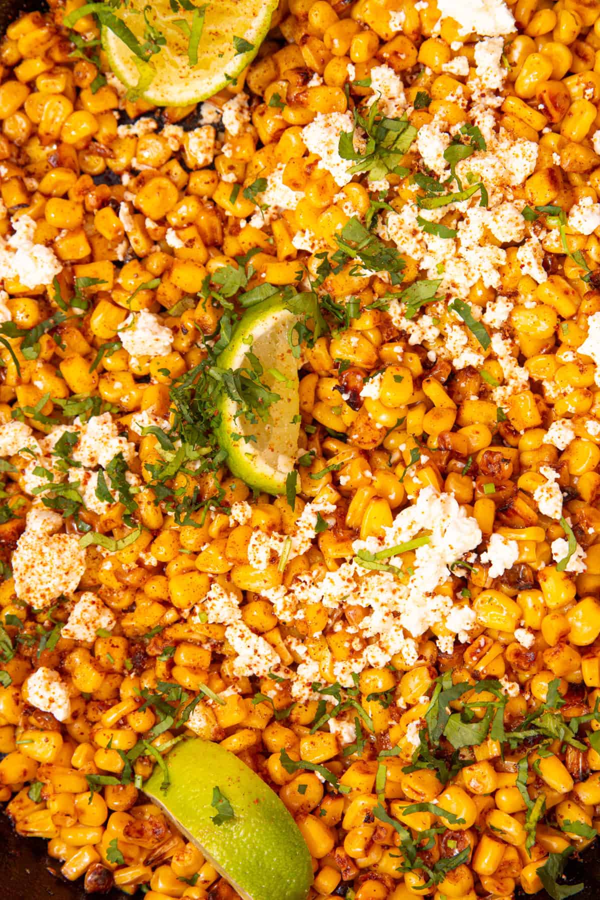 Close up of roasted sweet corn, topped with feta, corainder and lime wedges.