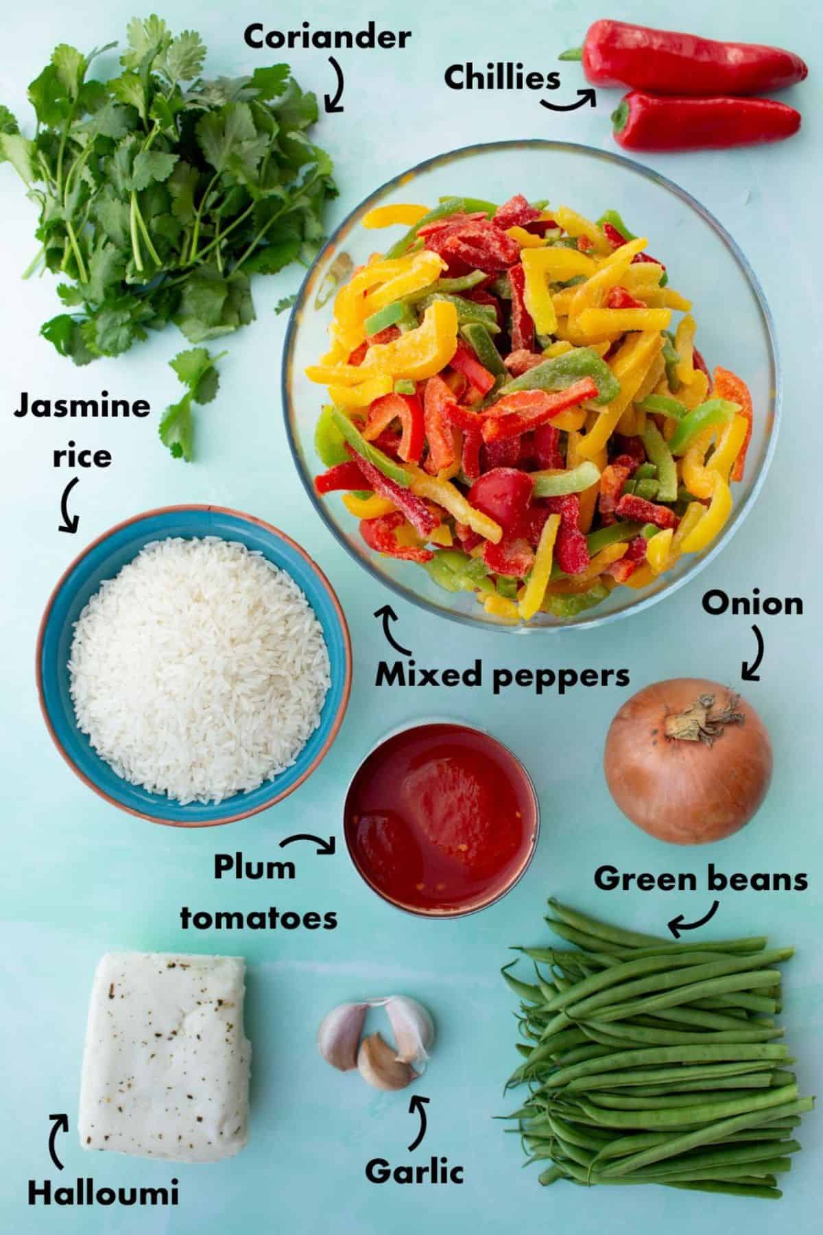 Ingredients to make the spicy tomato rice with halloiumi laid out on a pale blue background and labelled.
