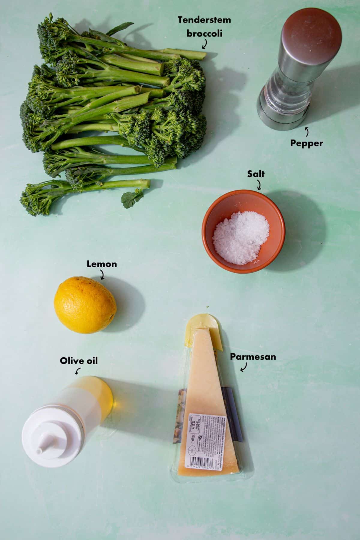 Ingredients to make roasted tenderstem broccoli laid out on a pale blue background and labelled.