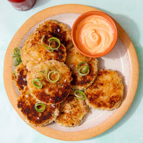 A plate with round browned fishcakes with soem dipping sauce and spring onion curls as decoration.
