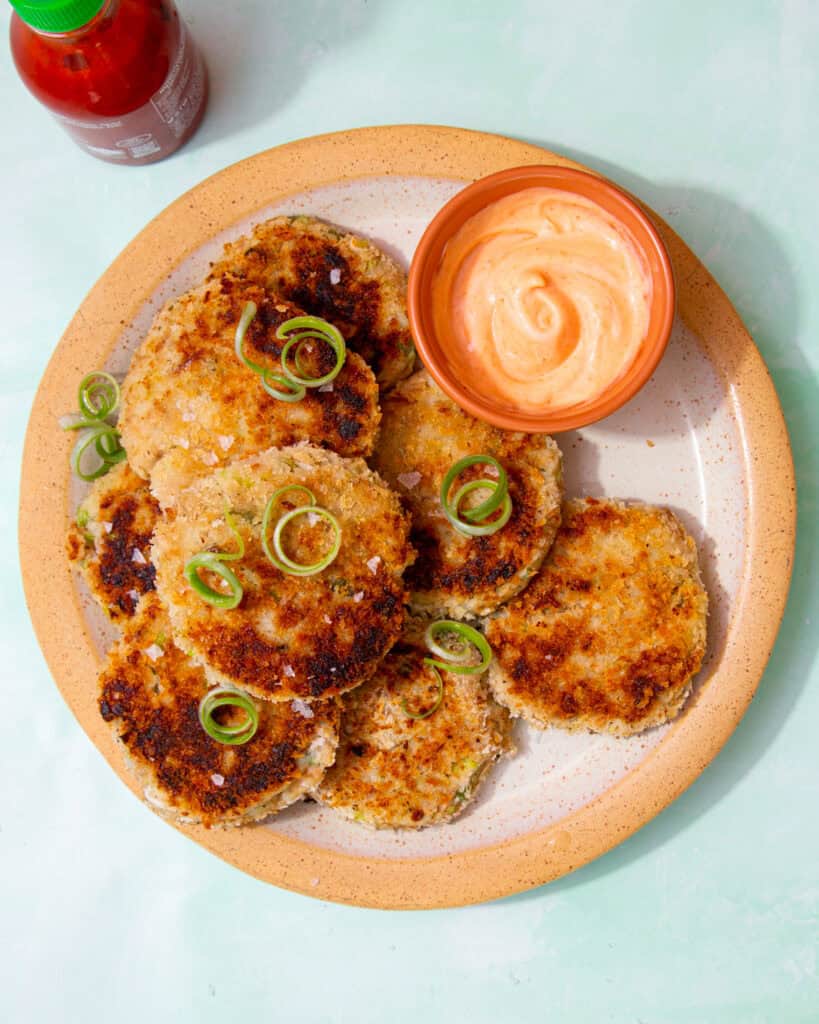 A plate with round browned fishcakes with soem dipping sauce and spring onion curls as decoration.