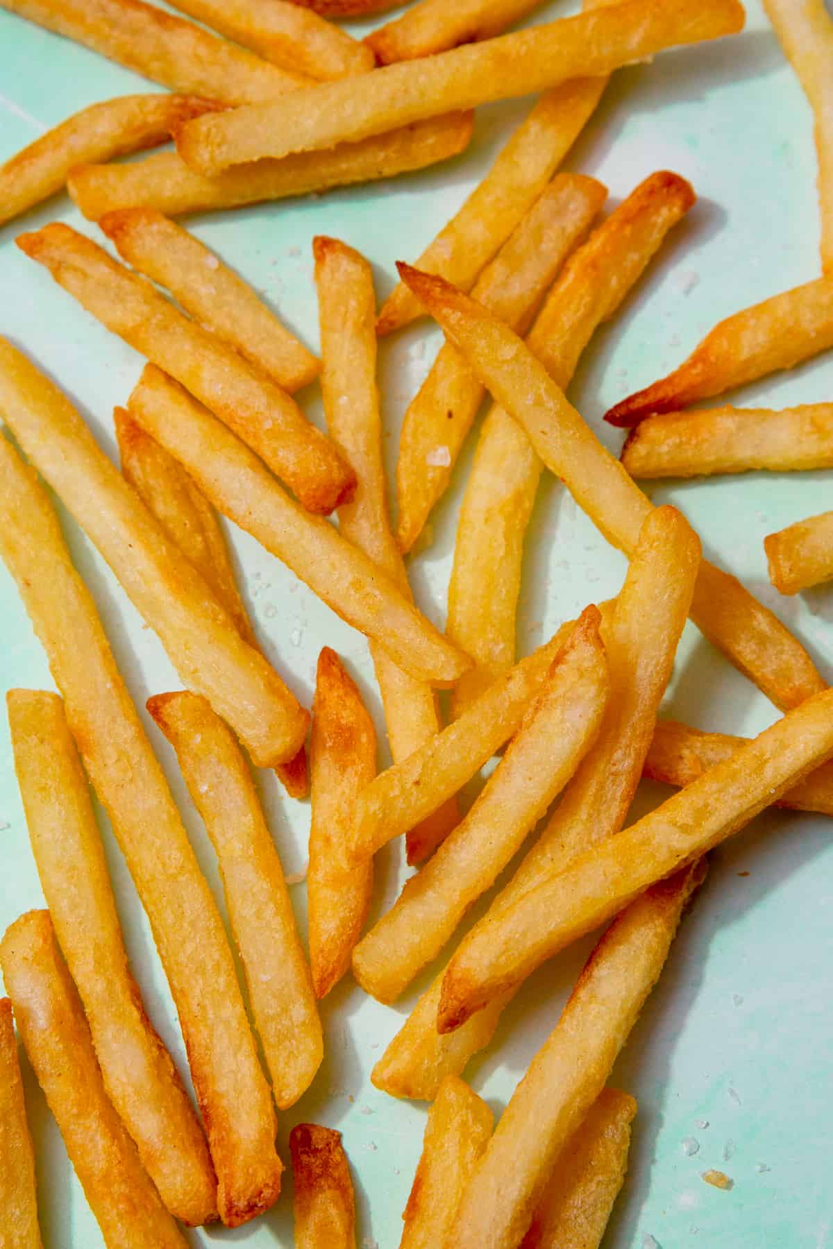 Golden browned Frence fries scattered over a pale blue background.