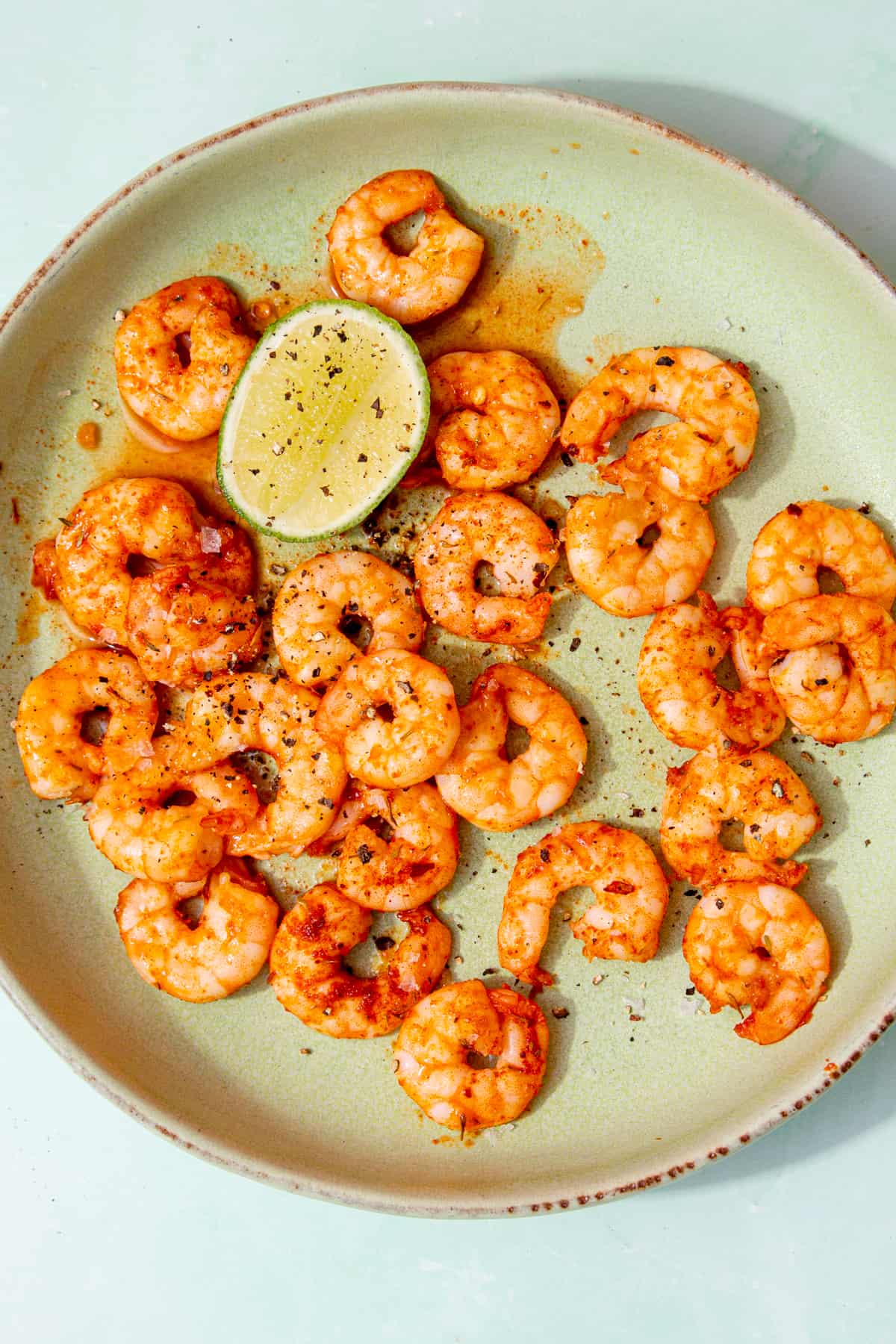 Seasoned King prawns in a bowl with a lime wedge and topped with some extra seasoning.