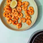 Cooked and seasoned aking prawns in a pale green bowl with a wedge of lime.