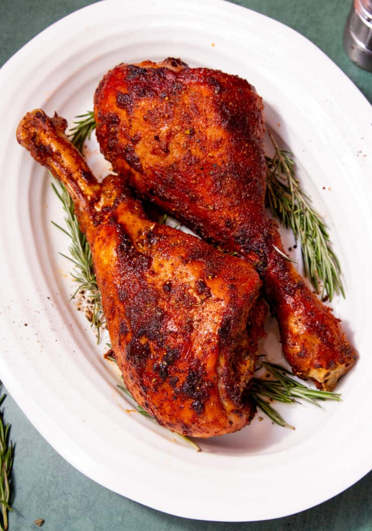 2 roasted turkey legs with some rosemary on a white oval plate.