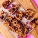 Breakfast oat bars with blueberries sliced on parchment paper on a wooden chopping board.