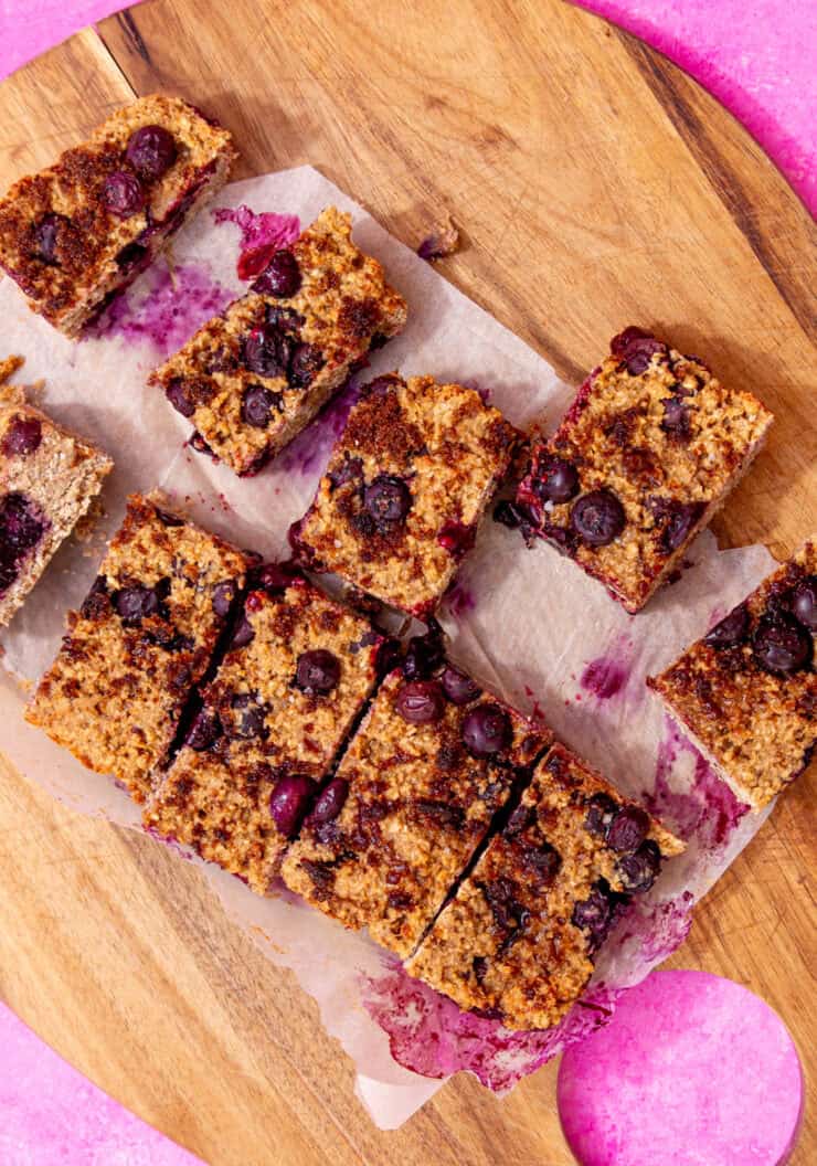 Breakfast oat bars with blueberries sliced on parchment paper on a wooden chopping board.