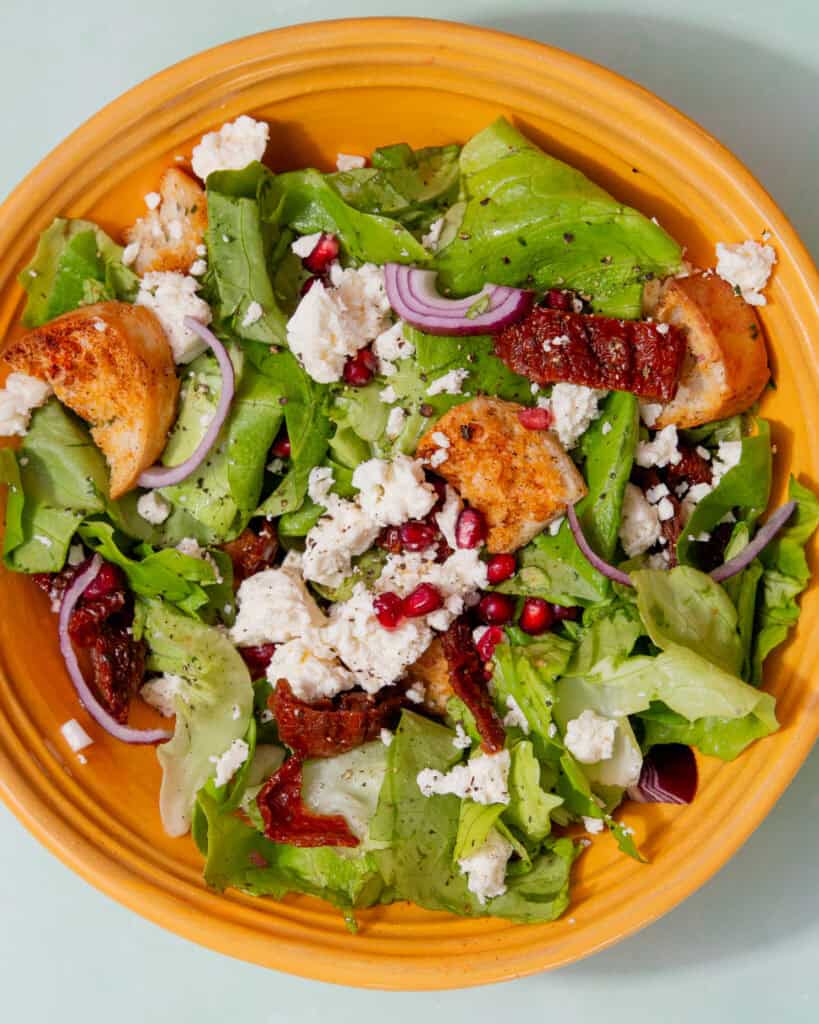 Feta and sun-dried tomato salad in a bowl with crumbled feta , lettuce and pomegranate.