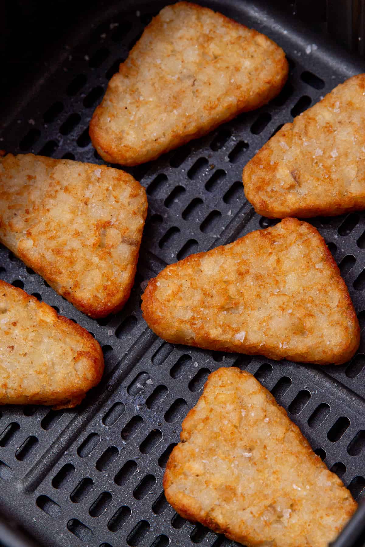 6 golden browned hash browns in the airfryer tray with a sprinkle of salt.