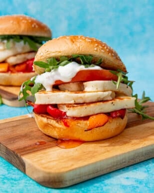 2 halloumi burger with lots of filling including tomatoes, lettuce, tzatziki and roasted peppers topped with a sesame bun.