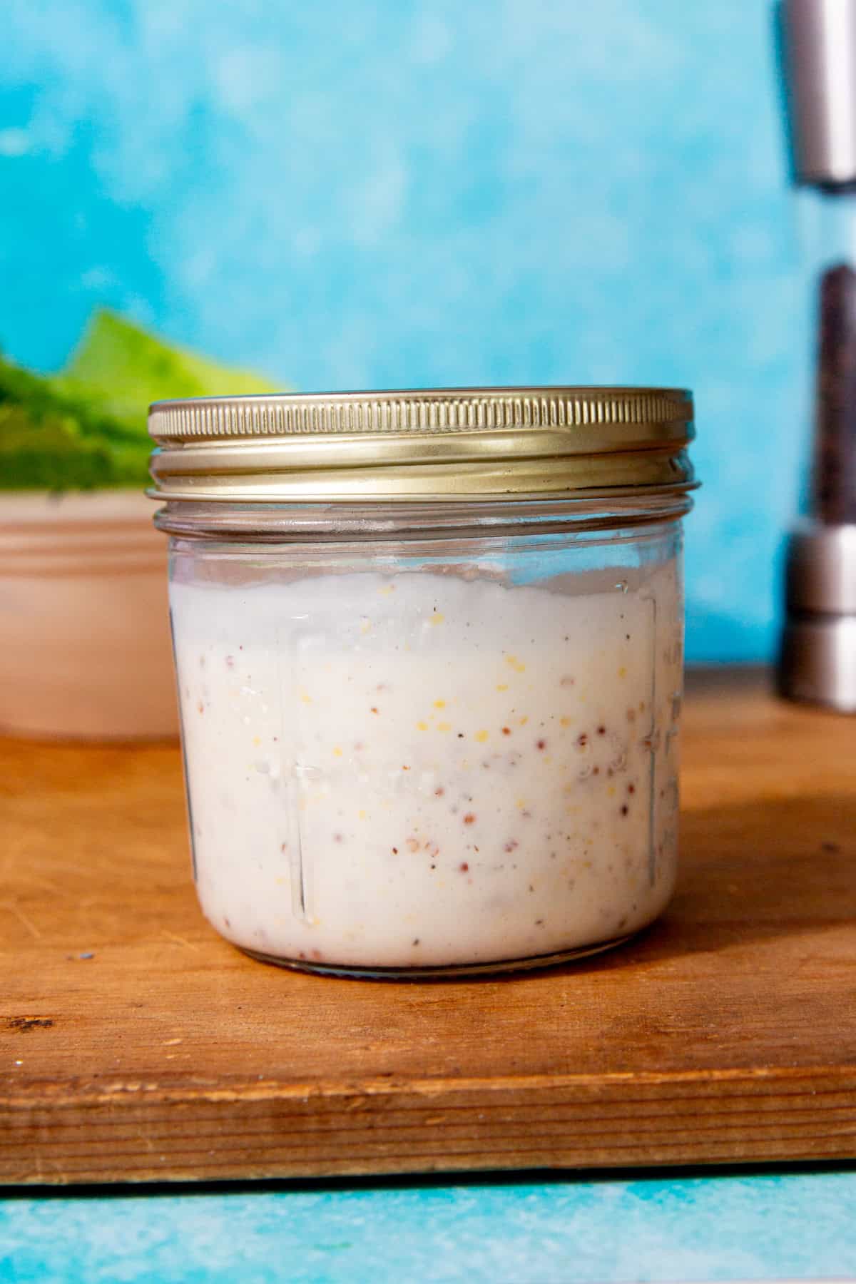 A mason jar with a lid on full of dressing with a both a salad in partial view behind.