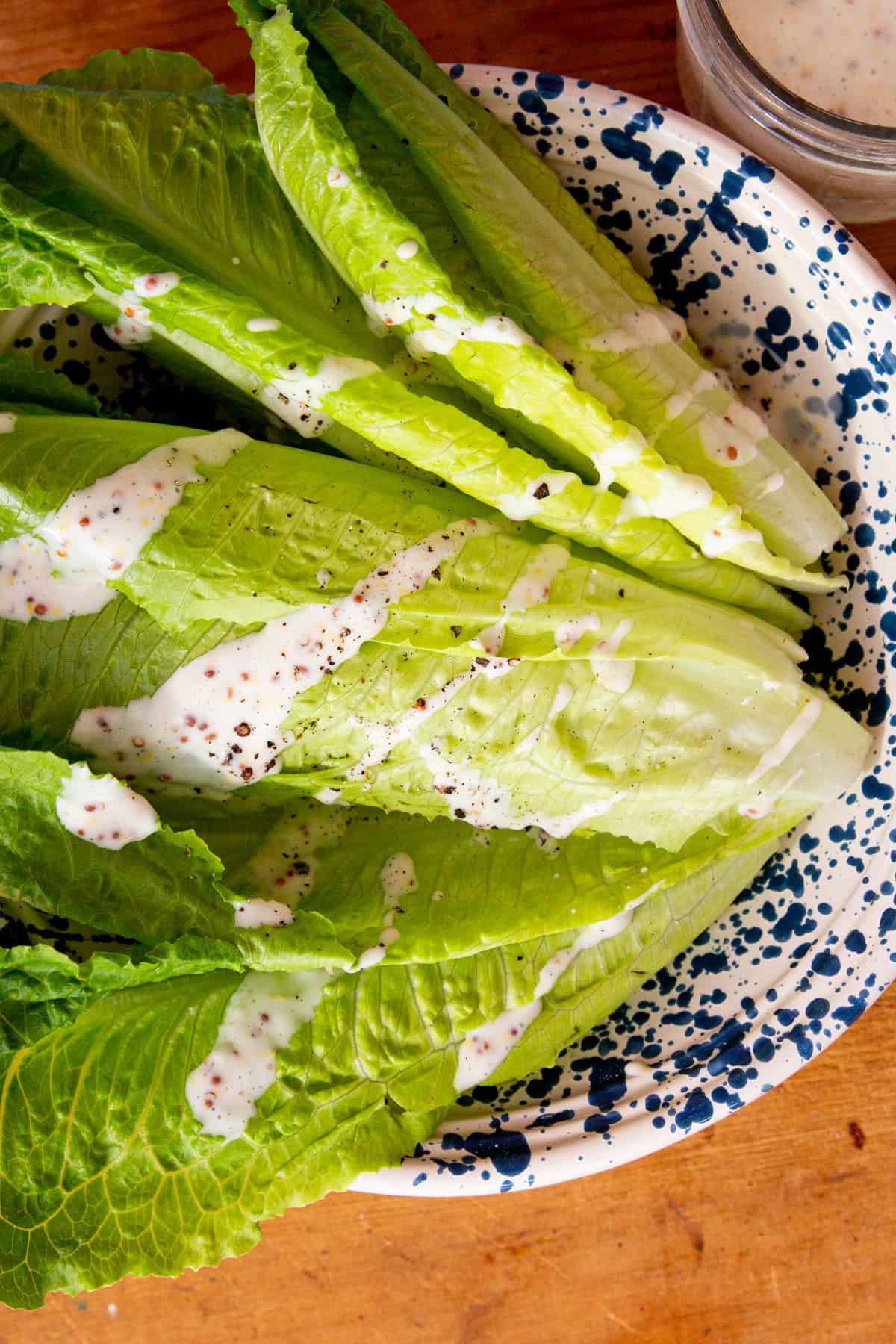 Romain lettcue leaves in a patterned bowl with slad dressing poured over in stripes.