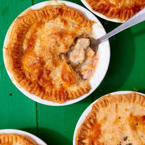 4 round white ramkins with chicken pot pies with golden browned pastry topping with a fork taking a portion out on one.