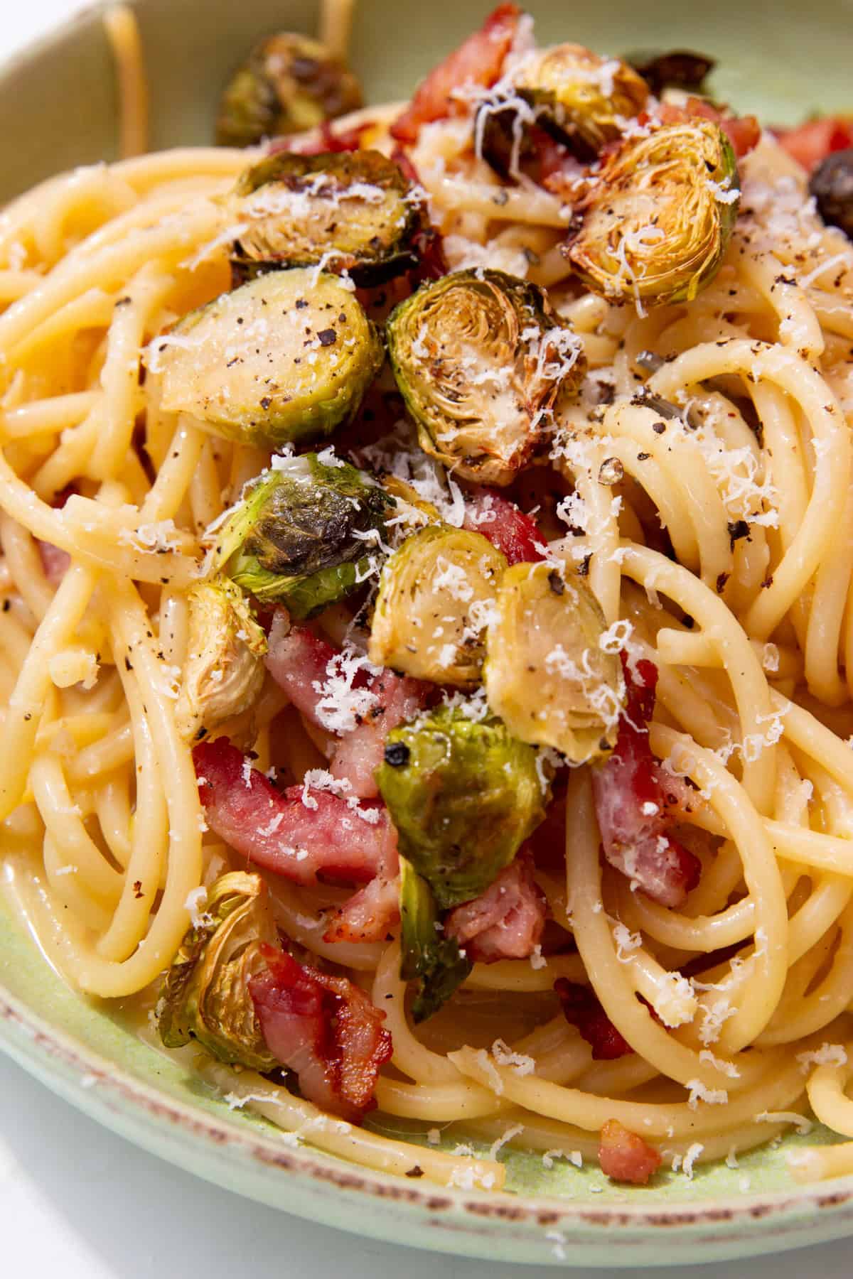Spaghetti with roasted Brussel sprouts, bacon and parmesan shavings in a bowl.