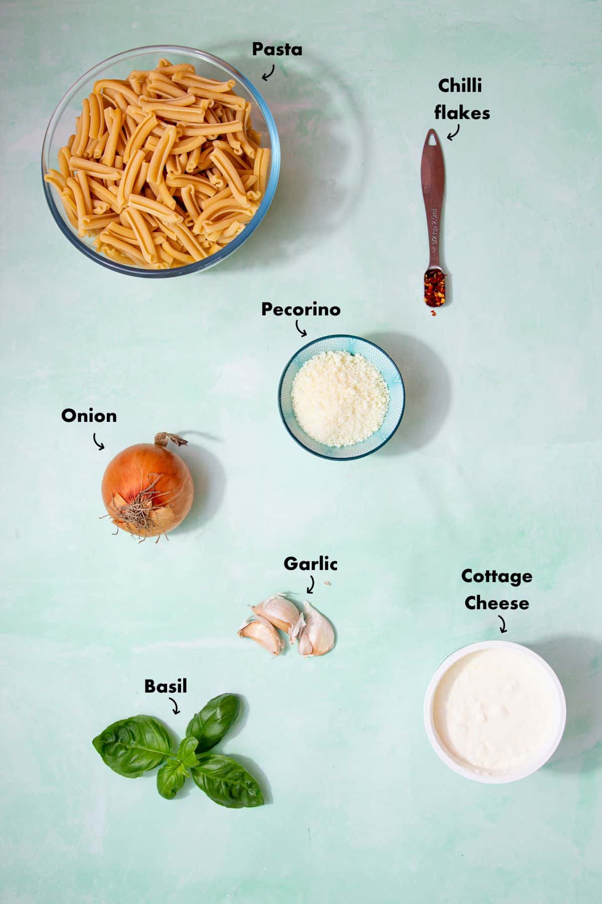 Ingredients to make cottage pie pasta laid out on a plae blue background and labelled.