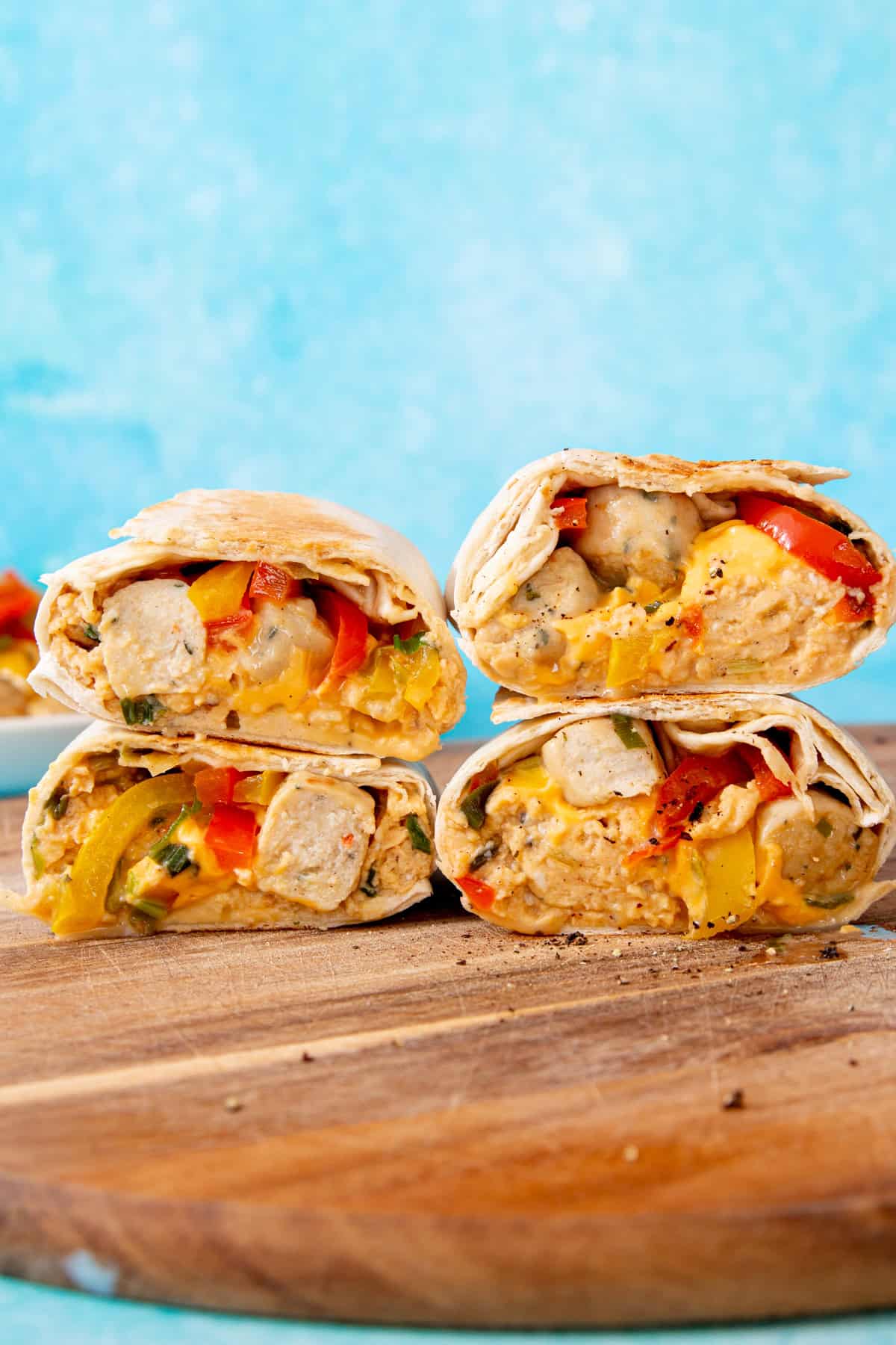 4 sliced through burritos with egg, peppers and sausage on a wooden board with a blue background.