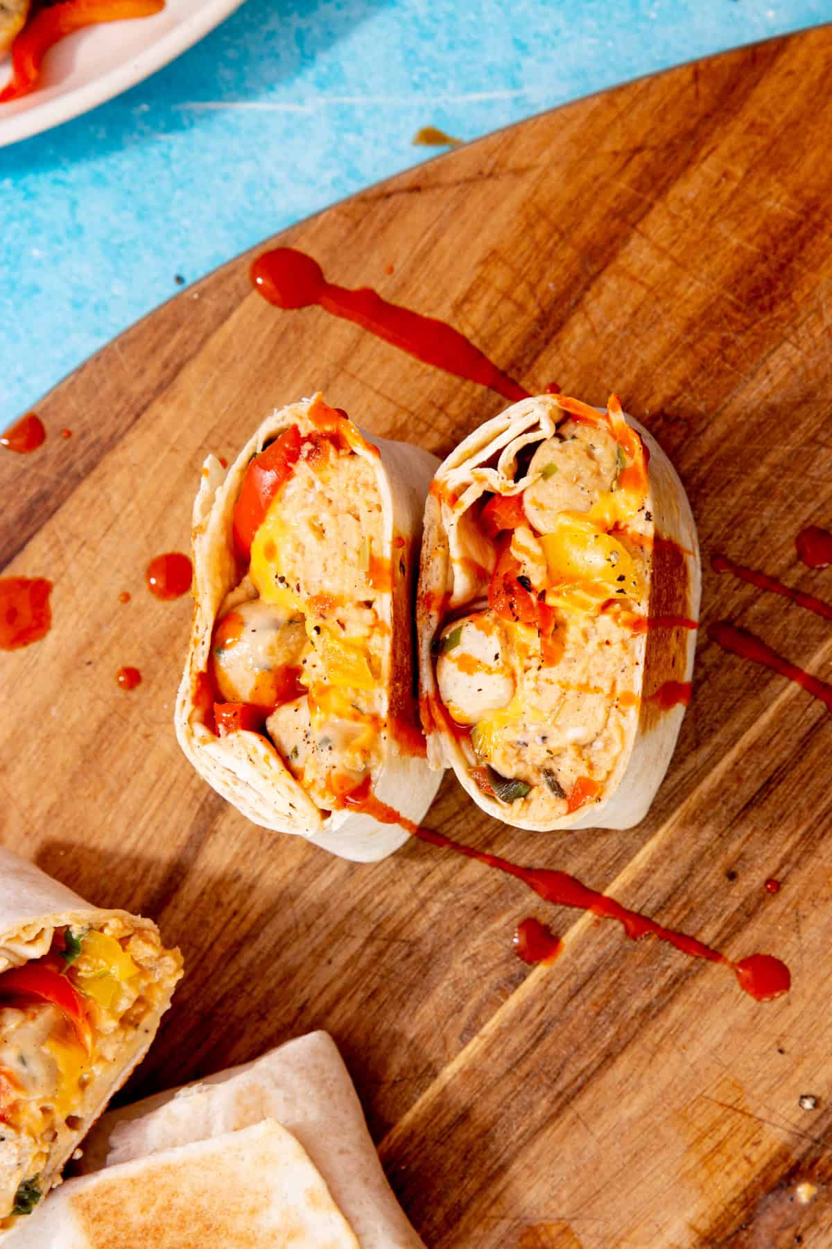 3 sliced through burritos with egg, peppers and sausage on a wooden board with a blue background with some tomato coloured sauce over top.