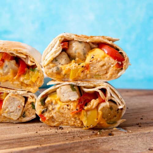 4 sliced burritos with egg, peppers and sausage on a wooden board with a blue background.