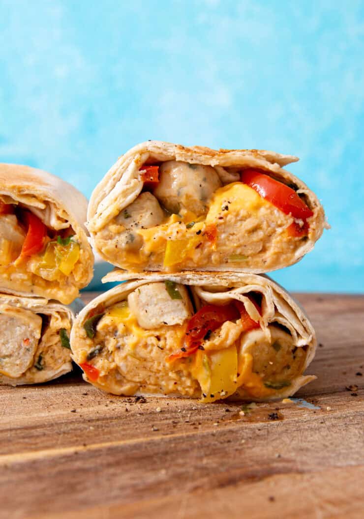 4 sliced burritos with egg, peppers and sausage on a wooden board with a blue background.