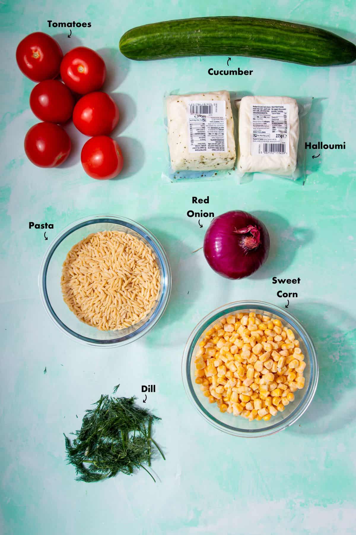 Ingredients to make the halloumi and orzo salad recipe laid out on a pale blue background and labelled.