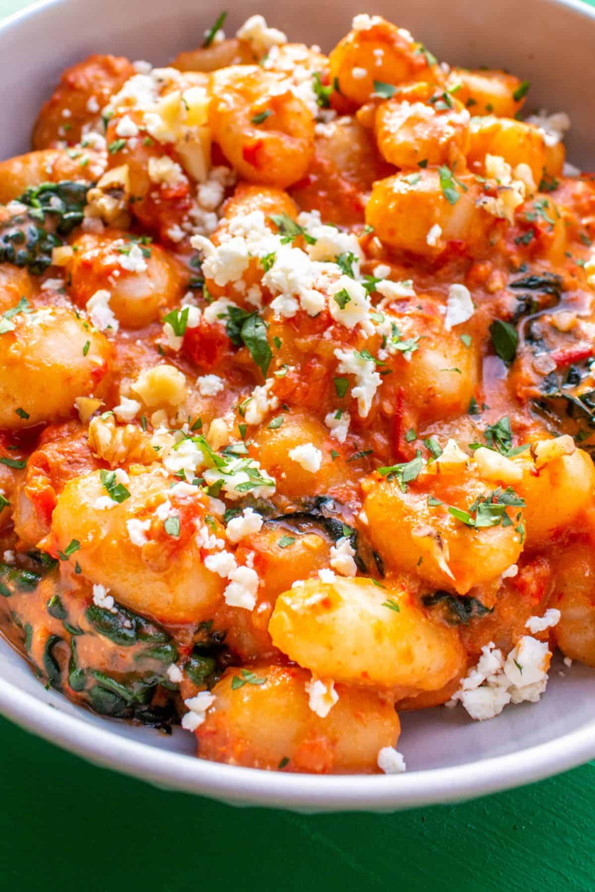 Gnocchi with a tomatoey sauce with some sprinkles of cheese and herbs in a bowl.