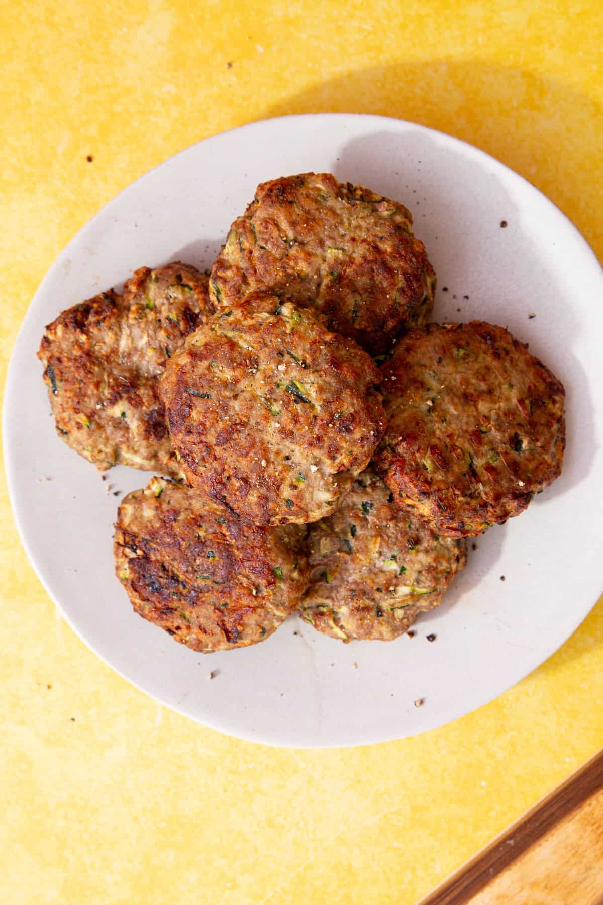 6 turkey burgers on a white plate on a yellow background.