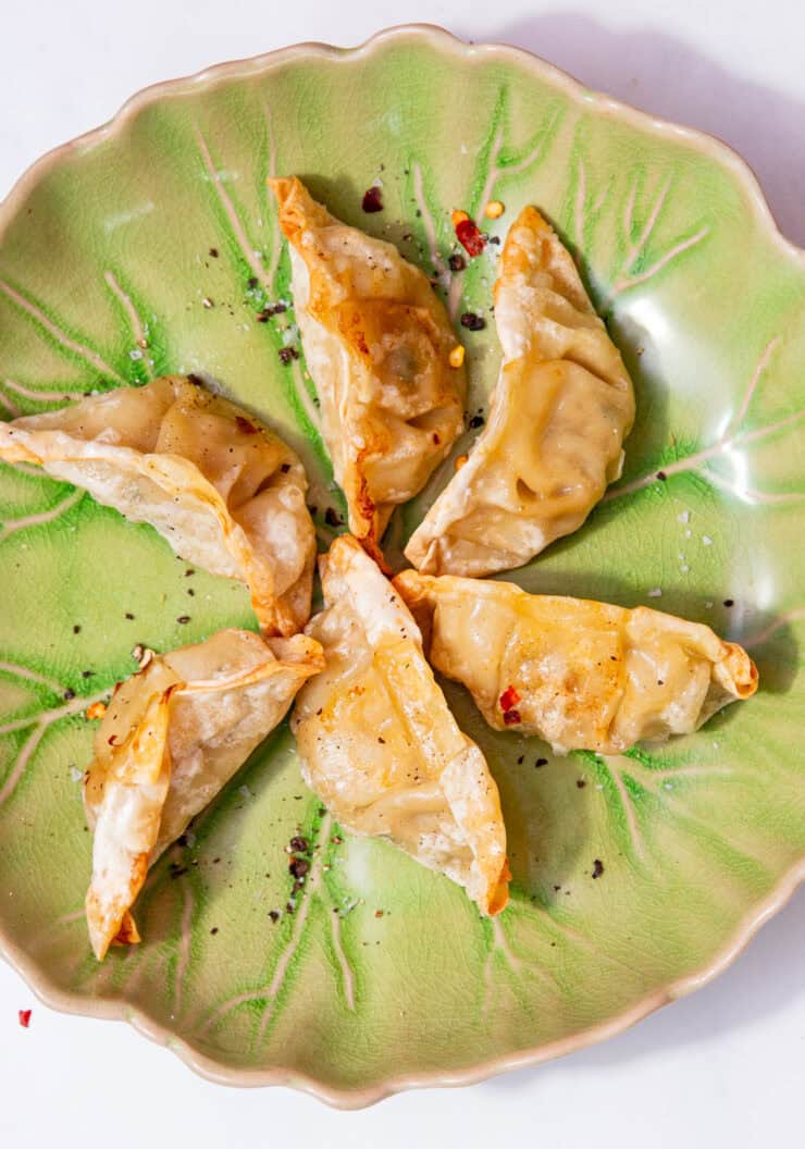 6 golden browned dumplings displayed on a plate with some chilli flakes.