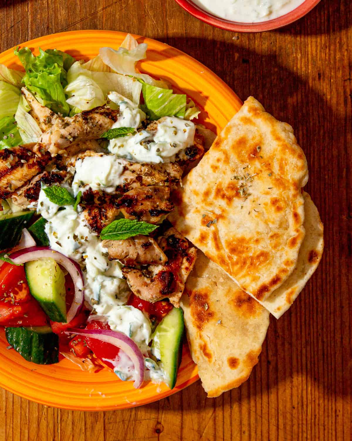 Quarter slices of flatbreads served with a plate of salad and chicken in a yellow bowl on a wooden table.
