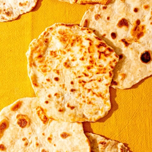 Lots of golden browned flatbreads on a yellowy coloured cloth.