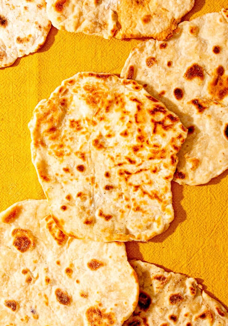 Lots of golden browned flatbreads on a yellowy coloured cloth.