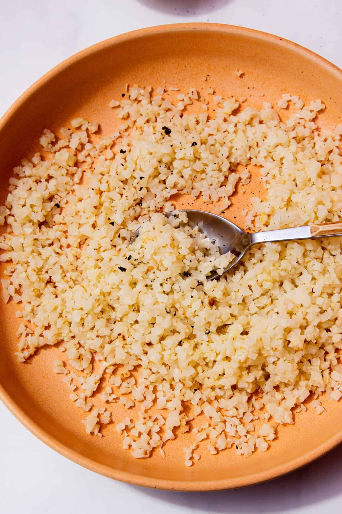 A pale tanned coloured bowl with cauliflower rice with a spoon.
