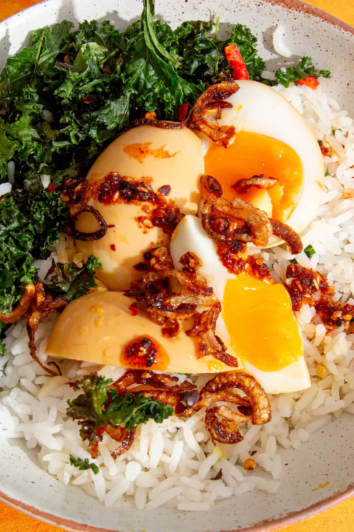 A bowl with eggs cut in quarters over rice with kale and roasted onions with chilli oil.