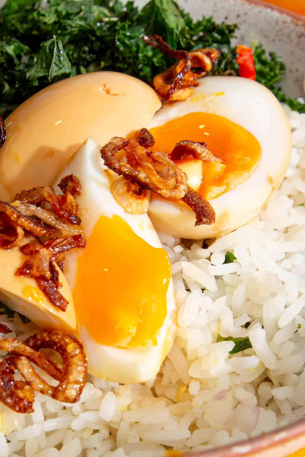Eggs with soft yolks cut in quarters over rice with kale and roasted onions with chilli oil.