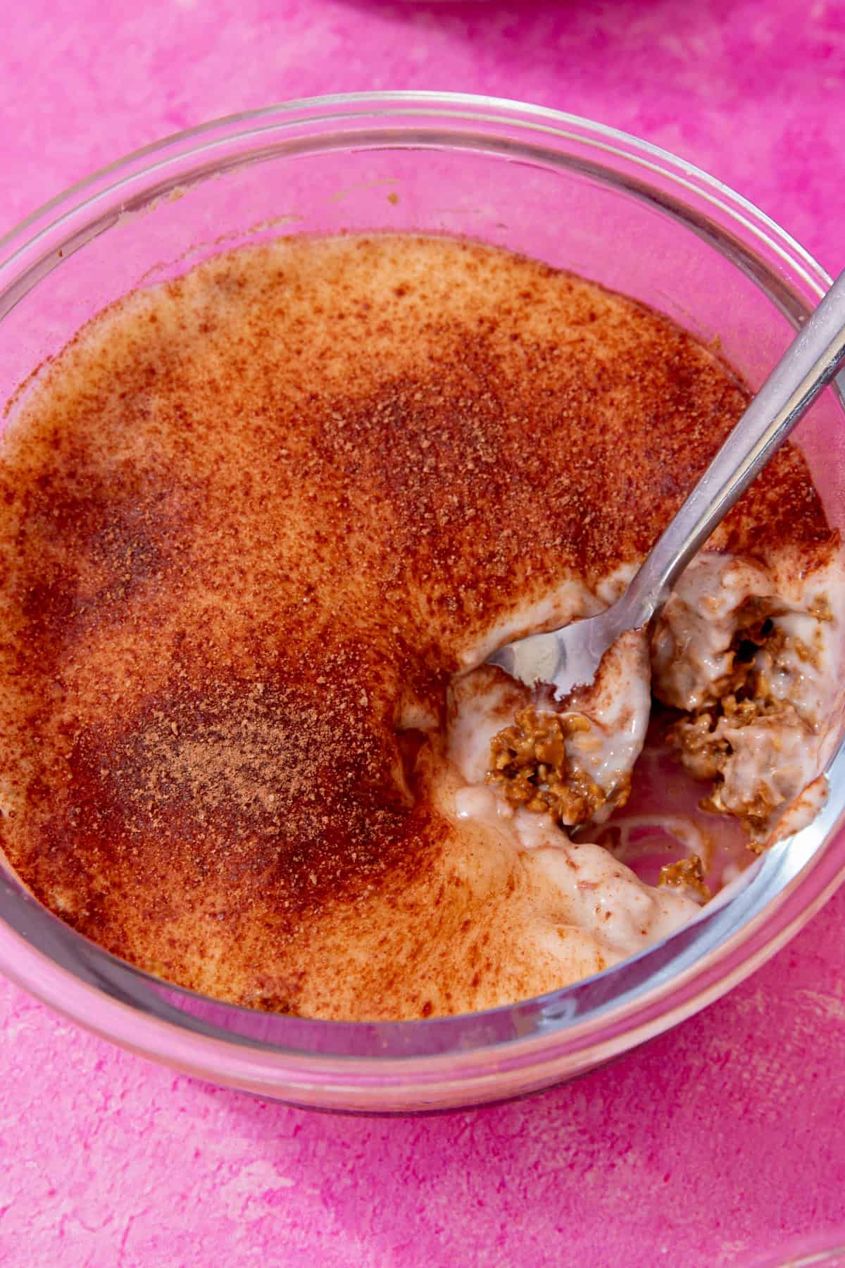 A glass bowl with oats and a yogurt topping with chocolate sprinkled over the top with a spoon taking a portion.