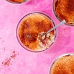 4 glass round bowls with breakfast oats, yogurt topped with sprinkling of chocolate on a pink background.