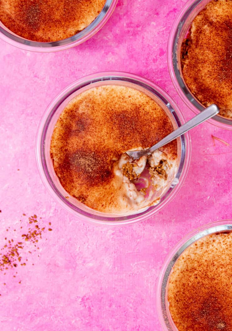 4 glass round bowls with breakfast oats, yogurt topped with sprinkling of chocolate on a pink background.