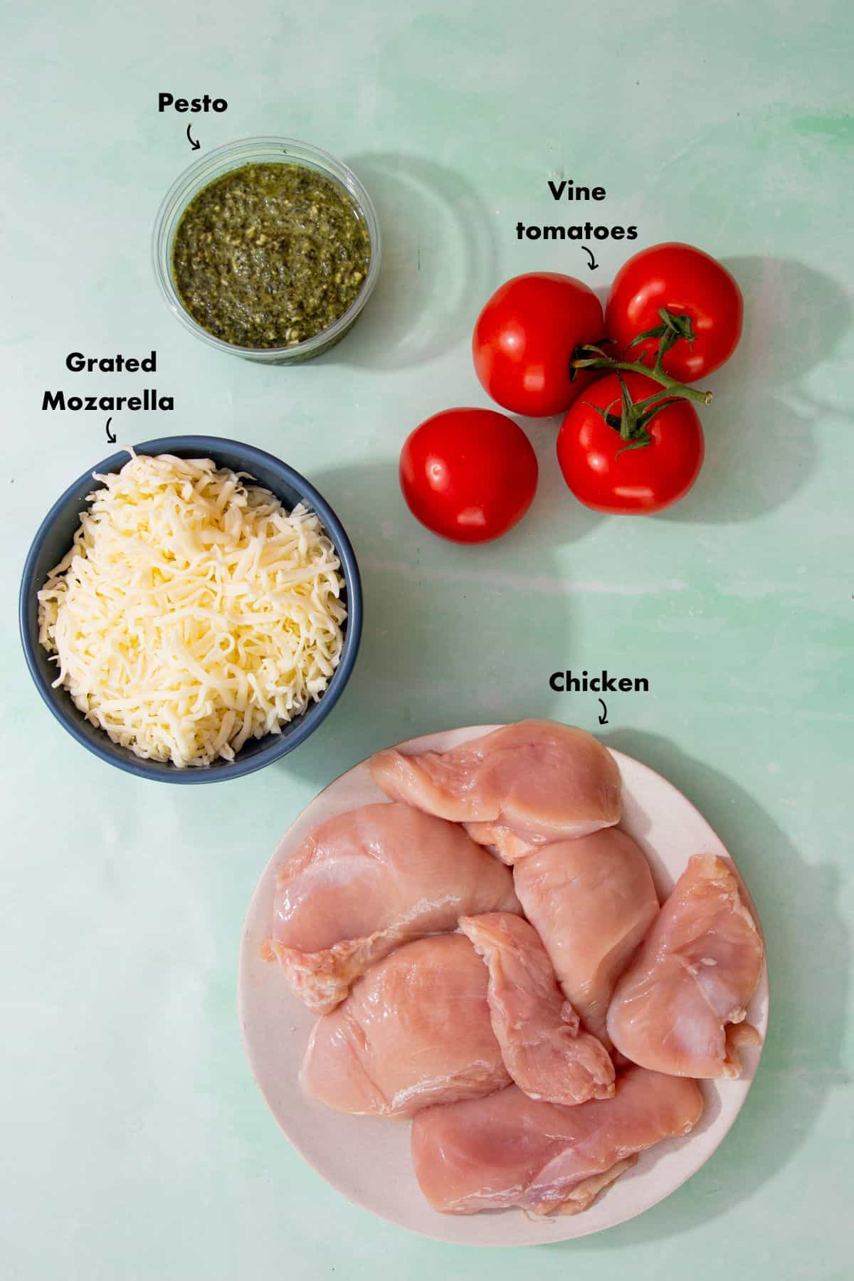 Ingredients to make the baked pesto chicken laid out on a pale blue background and labelled.