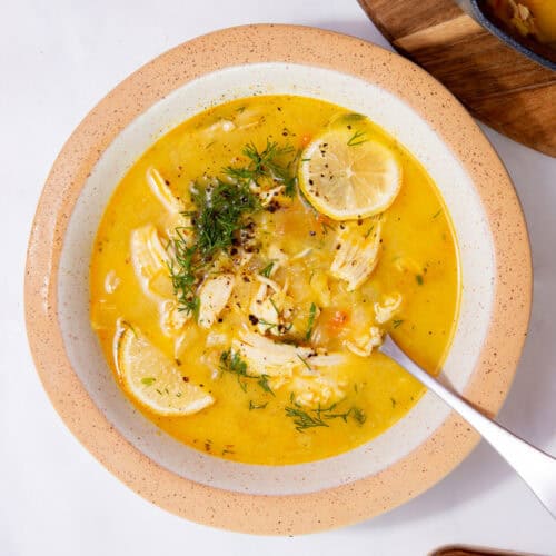 A bowl of chicken soup with lemon slices and dill on a white background.