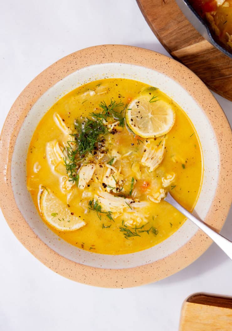 A bowl of chicken soup with lemon slices and dill on a white background.