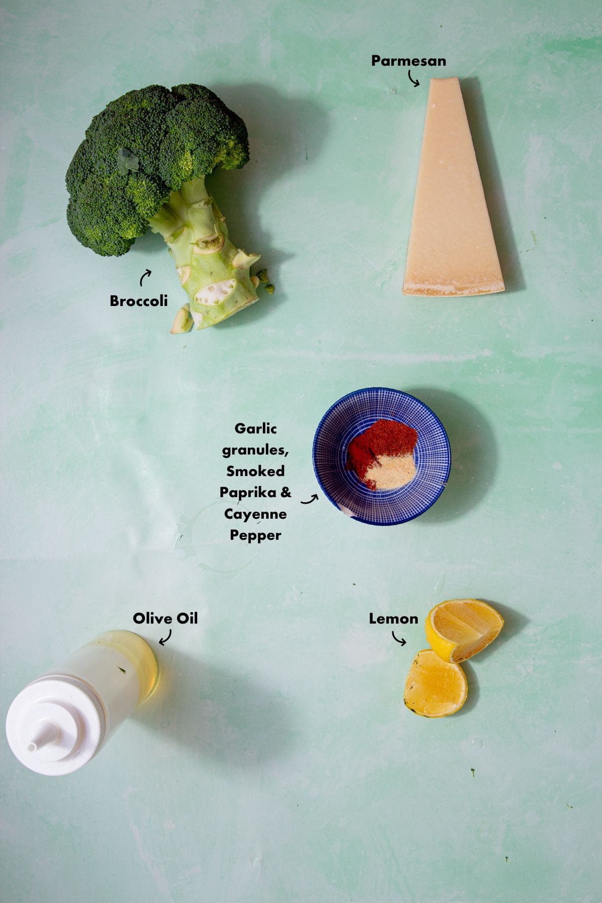 Ingredients to make the smashed broccoli recipe laid out on a plae blue background and labelled.