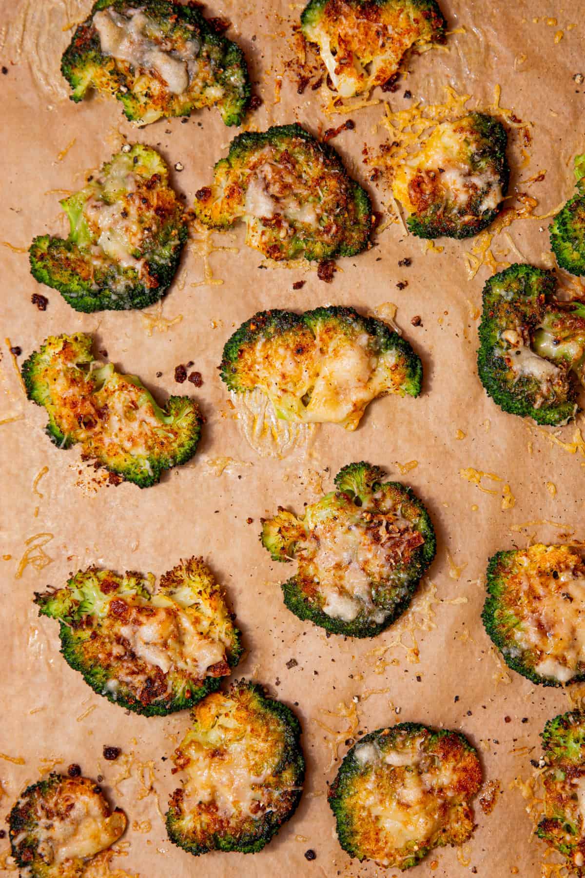 Baked golden browned broccoli florets  covered in some cheese on some brown parchment paper.