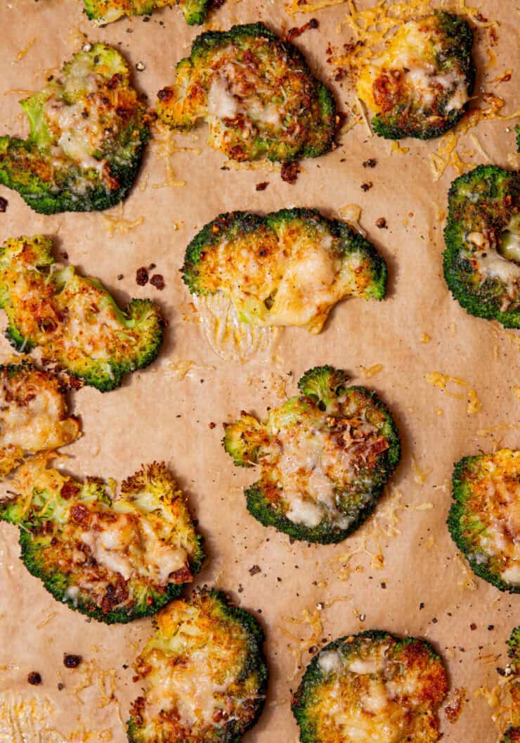 Lots of baked golden browned broccoli florets covered in some cheese scattered over some brown parchment paper.