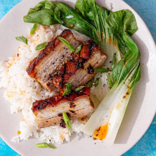 3 slices of golden bowned pork on a bed of rice with pac choi on a blue background.