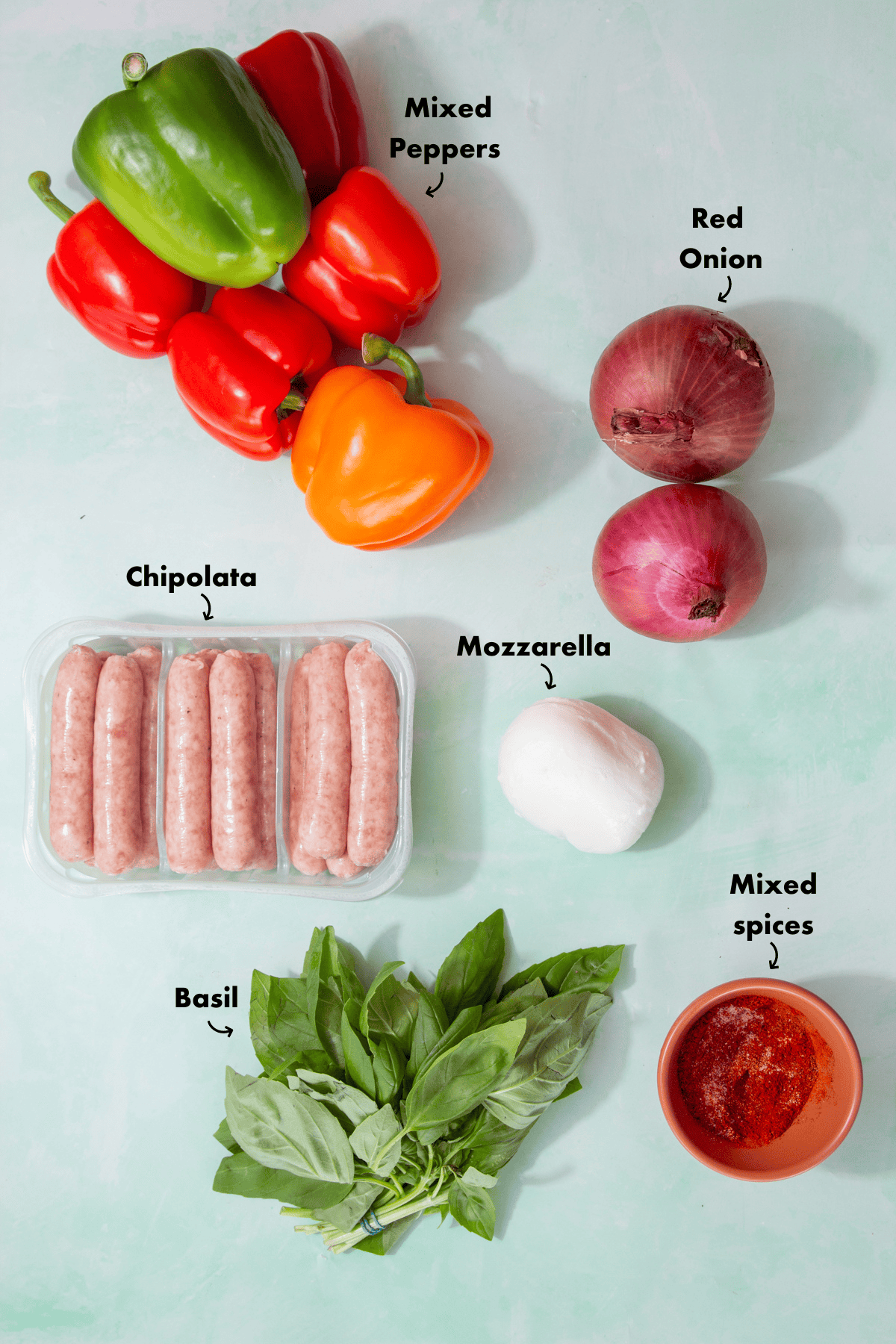 Ingredients to make the sausage and peppers recipe laid out on a pale blue background and labelled.